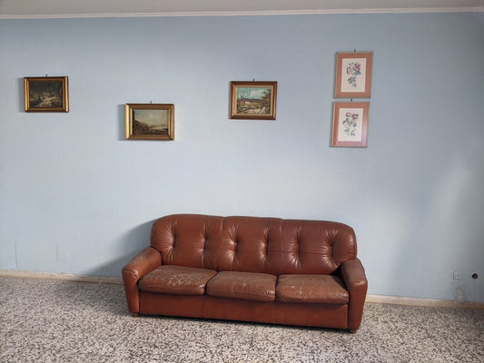 a brown leather couch in a room with pictures on the wall