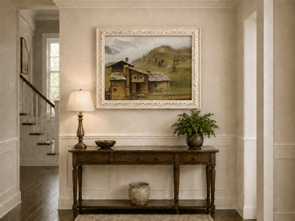 Framed hand-painted alpine landscape oil painting with a chalet, pasture and bell tower displayed above an entryway console table.