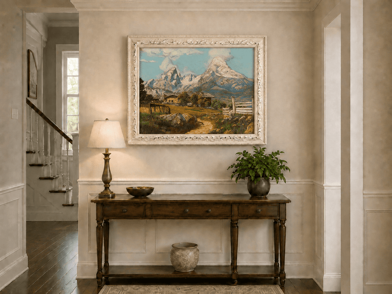 Framed hand-painted alpine farmhouse oil painting beneath distant snow-capped peaks displayed above an entryway console table.