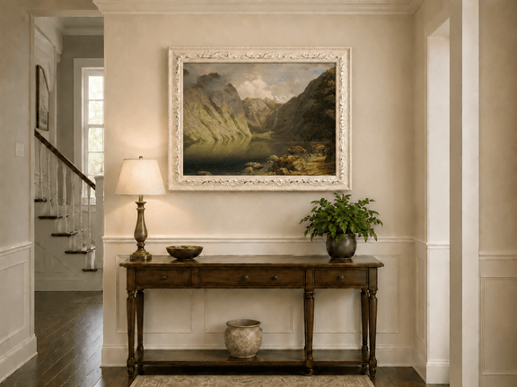 Framed hand-painted alpine lake valley oil painting with a waterfall and rugged mountains displayed above an entryway console table.