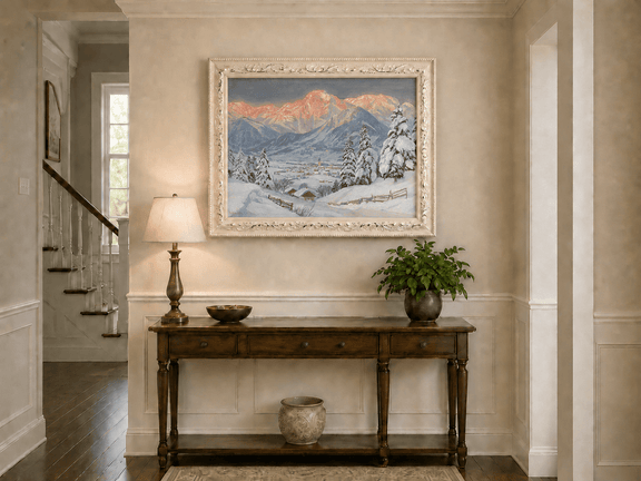 Framed hand-painted alpine town oil painting beneath glowing pink mountain peaks displayed above an entryway console table.