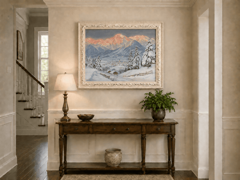 Framed hand-painted alpine town oil painting beneath glowing pink mountain peaks displayed above an entryway console table.