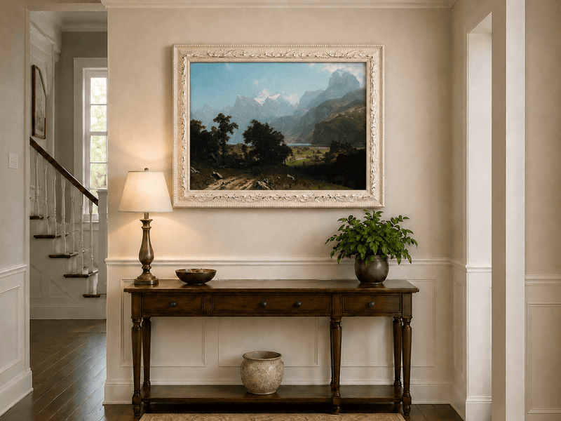 Framed hand-painted alpine valley oil painting with a lake and layered mountain peaks displayed above an entryway console table.