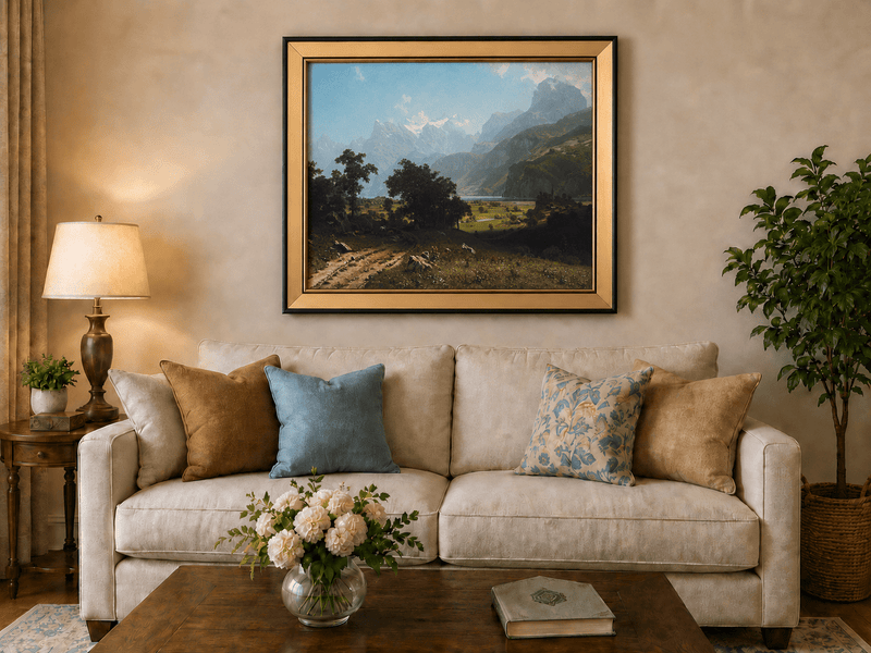 Framed hand-painted alpine valley oil painting with a lake and layered mountain peaks displayed above a neutral living room sofa.