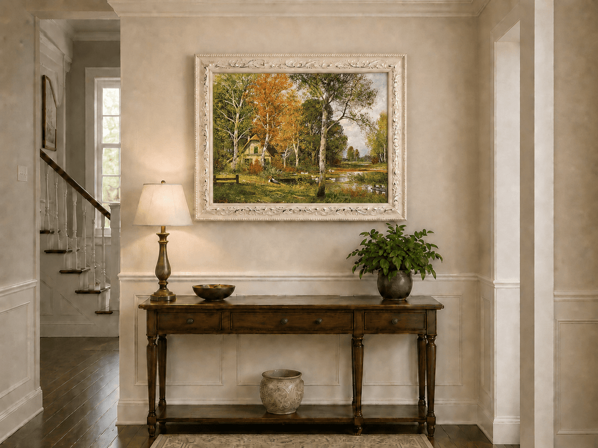 Framed hand-painted autumn riverside oil painting with a cottage among golden birch trees displayed above an entryway console table.