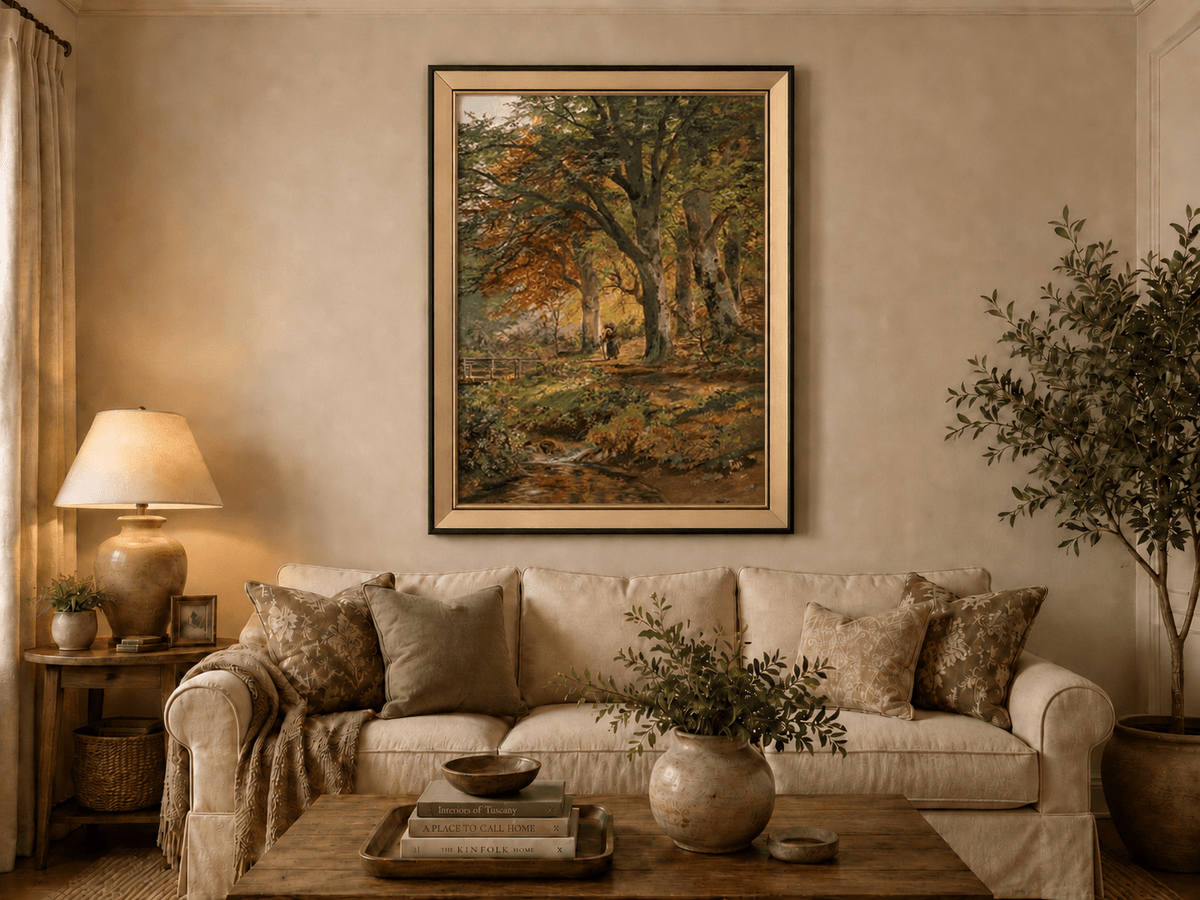 Framed hand-painted autumn forest oil painting with a leaf-covered path beside a stream displayed above a neutral living room sofa.