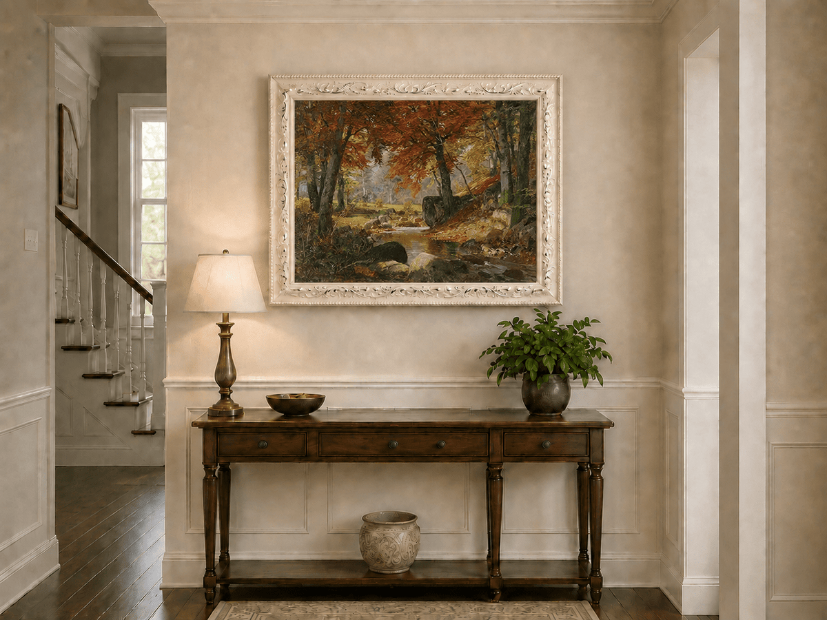 Framed hand-painted autumn forest stream oil painting flowing around mossy boulders displayed above an entryway console table.