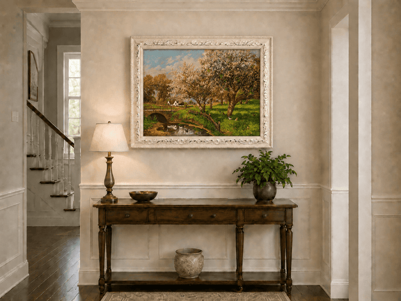 Framed hand-painted blooming orchard oil painting with a stone bridge over a country stream displayed above an entryway console table.