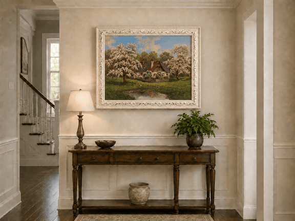 Framed hand-painted spring cottage oil painting surrounded by blossoming trees beside a quiet pond displayed above an entryway console table.