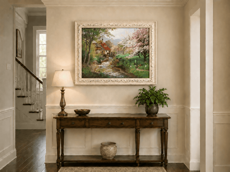 Framed hand-painted spring mill house oil painting beside a flower-lined woodland stream displayed above an entryway console table.