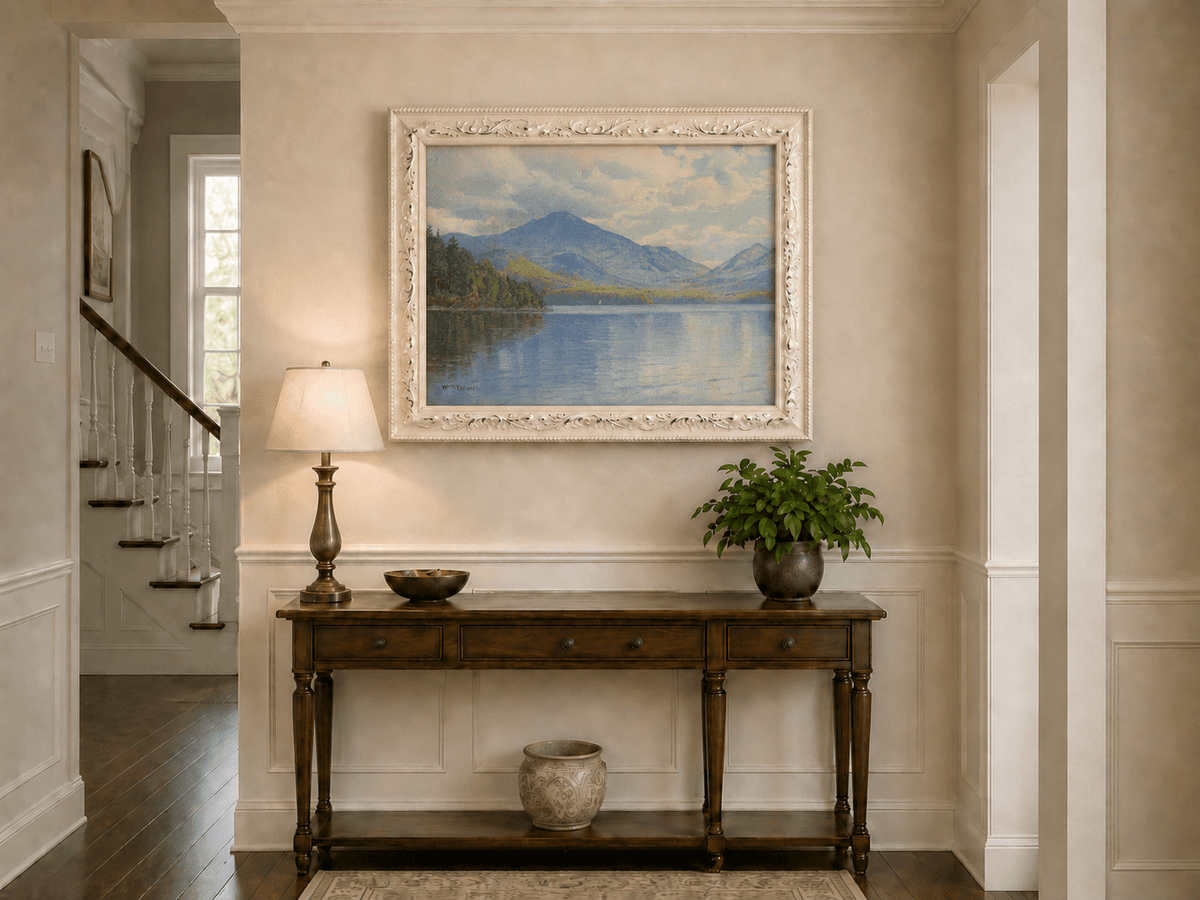 Framed hand-painted lake oil painting with calm reflections and a forested shoreline displayed above an entryway console table.
