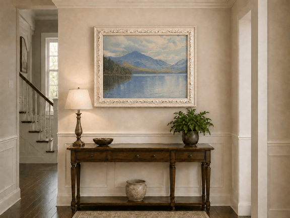 Framed hand-painted lake oil painting with calm reflections and a forested shoreline displayed above an entryway console table.