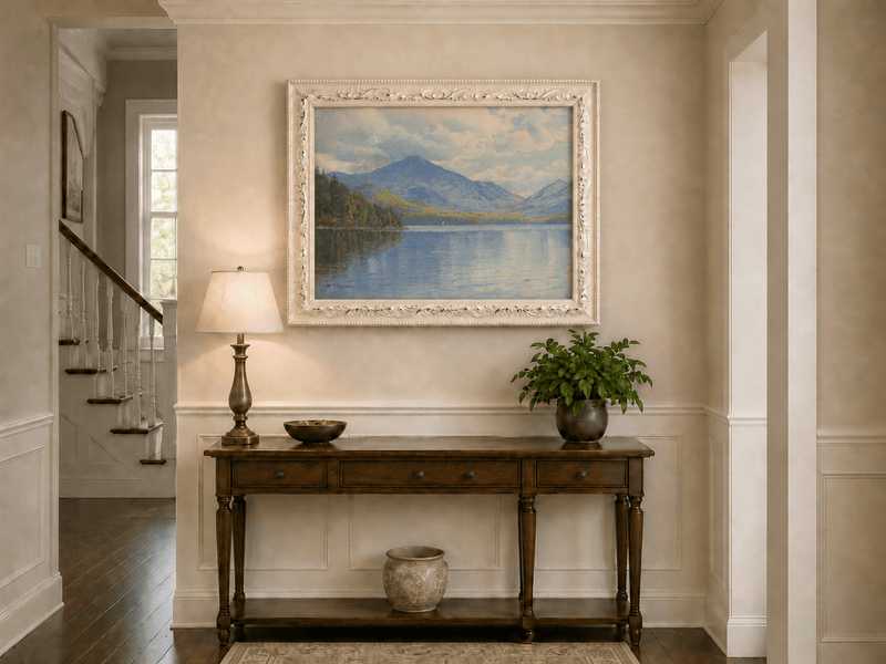 Framed hand-painted lake oil painting with calm reflections and a forested shoreline displayed above an entryway console table.