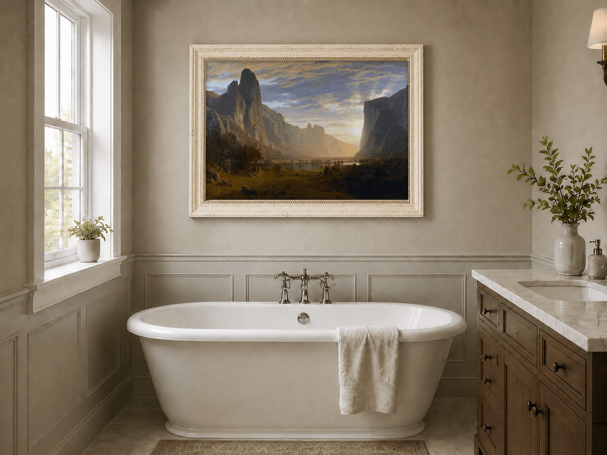 Framed hand-painted cliffs and river oil painting illuminated by warm golden light displayed above a freestanding bathtub.