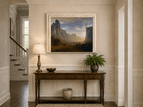 Framed hand-painted cliffs and river oil painting illuminated by warm golden light displayed above an entryway console table.