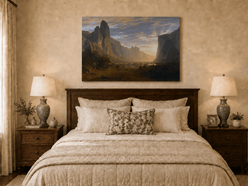 Unframed hand-painted cliffs and river oil painting illuminated by warm golden light displayed above a wooden bed in a neutral bedroom.