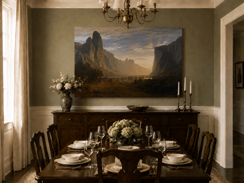 Unframed hand-painted cliffs and river oil painting illuminated by warm golden light displayed above a formal dining table.