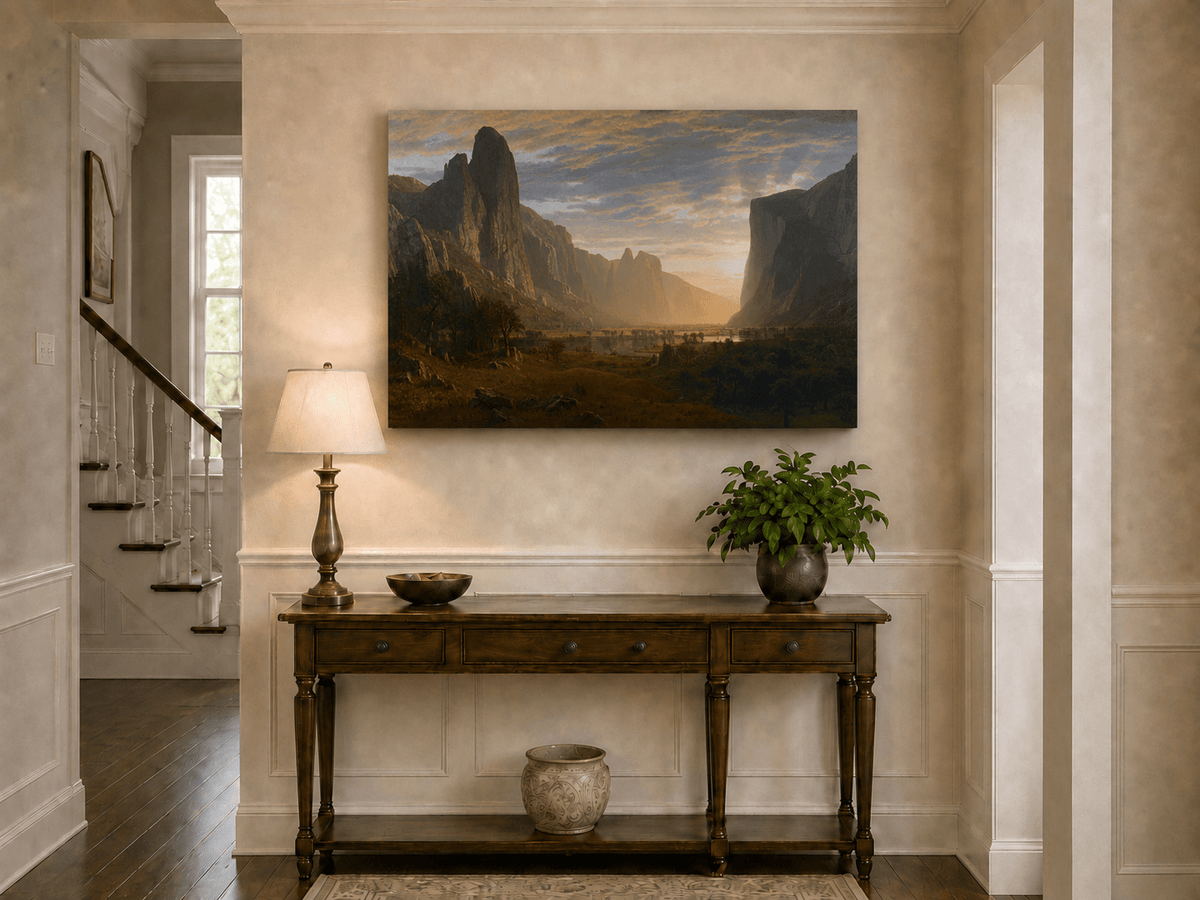 Unframed hand-painted cliffs and river oil painting illuminated by warm golden light displayed above an entryway console table.