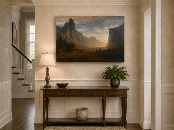 Unframed hand-painted cliffs and river oil painting illuminated by warm golden light displayed above an entryway console table.