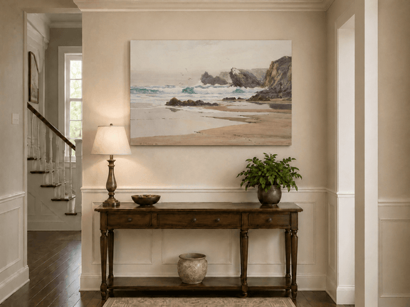Unframed hand-painted coastal beach oil painting with crashing waves and cliffside rocks displayed above an entryway console table.