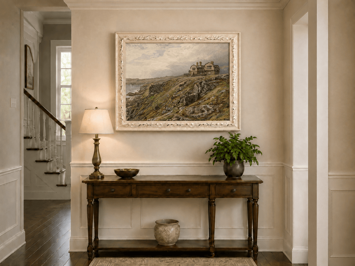 Framed hand-painted coastal oil painting with a cliff house, rocky slopes and seaside view displayed above an entryway console table.