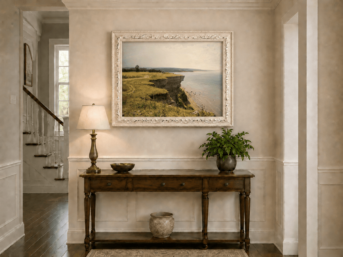 Framed hand-painted coastal landscape oil painting with a grassy cliff and expansive sea view displayed above an entryway console table.