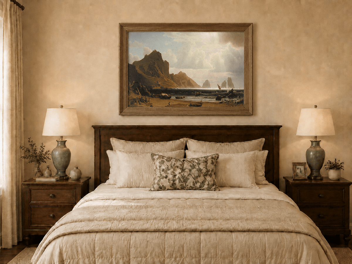 Framed hand-painted coastal cliffs oil painting with fishing boats and figures on a rocky beach displayed above a wooden bed in a neutral bedroom.