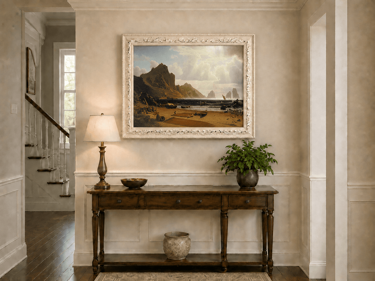 Framed hand-painted coastal cliffs oil painting with fishing boats and figures on a rocky beach displayed above an entryway console table.