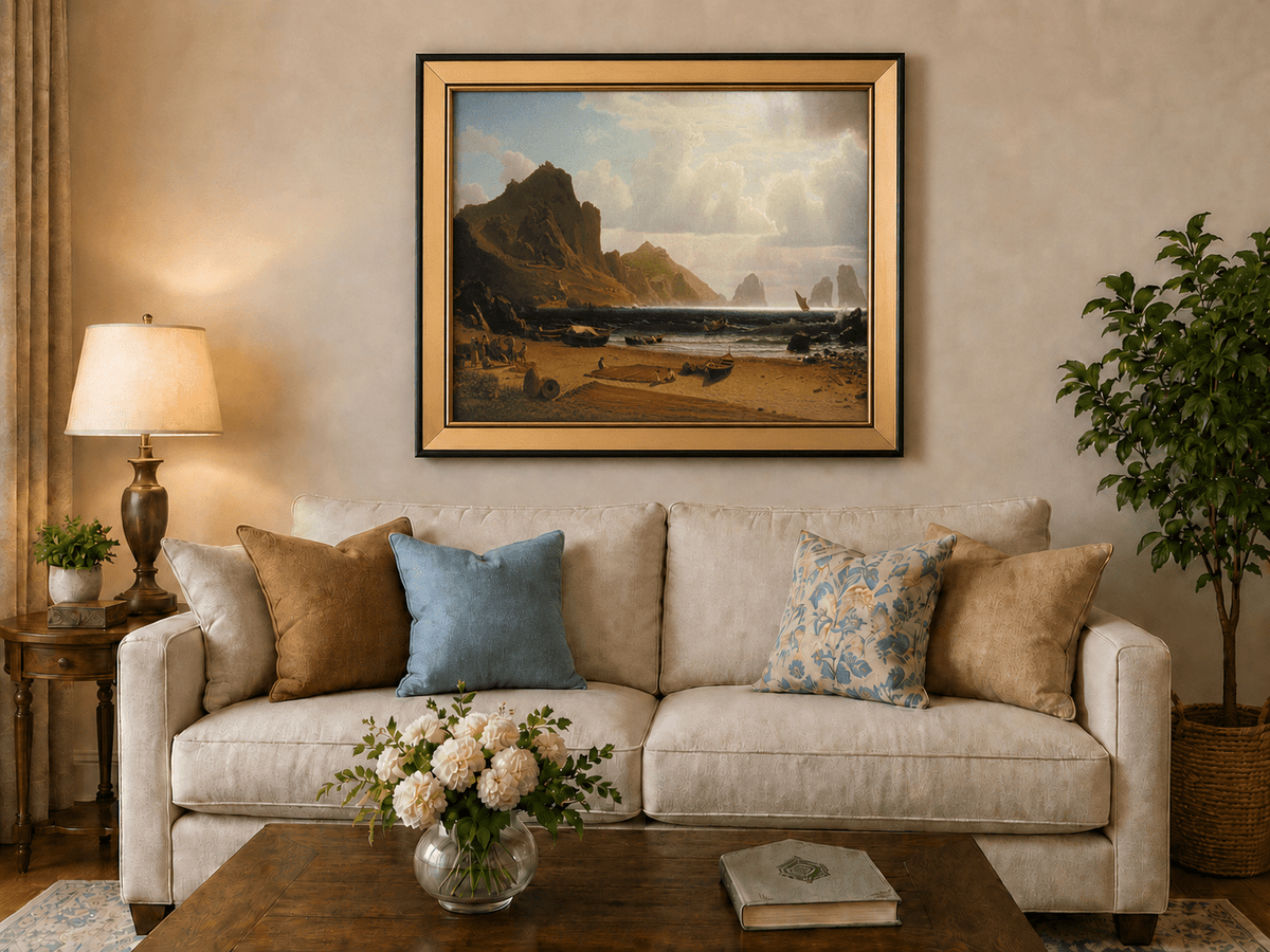 Framed hand-painted coastal cliffs oil painting with fishing boats and figures on a rocky beach displayed above a neutral living room sofa.