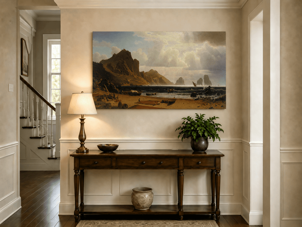 Unframed hand-painted coastal cliffs oil painting with fishing boats and figures on a rocky beach displayed above an entryway console table.