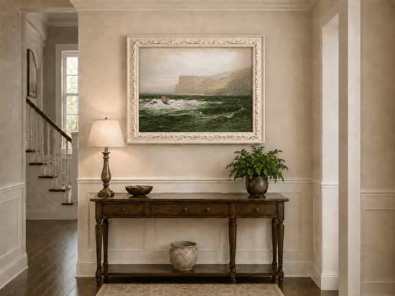 Framed hand-painted seascape oil painting with coastal cliffs, crashing waves and a seaside rock displayed above an entryway console table.