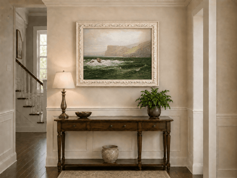 Framed hand-painted seascape oil painting with coastal cliffs, crashing waves and a seaside rock displayed above an entryway console table.