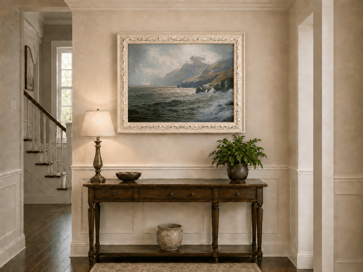Framed hand-painted coastal mountain oil painting with waves breaking on a rocky shore displayed above an entryway console table.