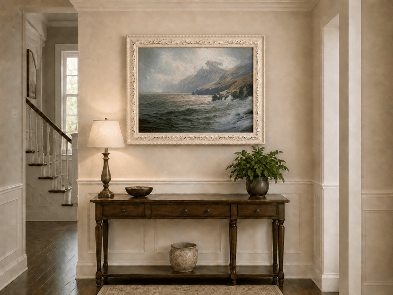 Framed hand-painted coastal mountain oil painting with waves breaking on a rocky shore displayed above an entryway console table.