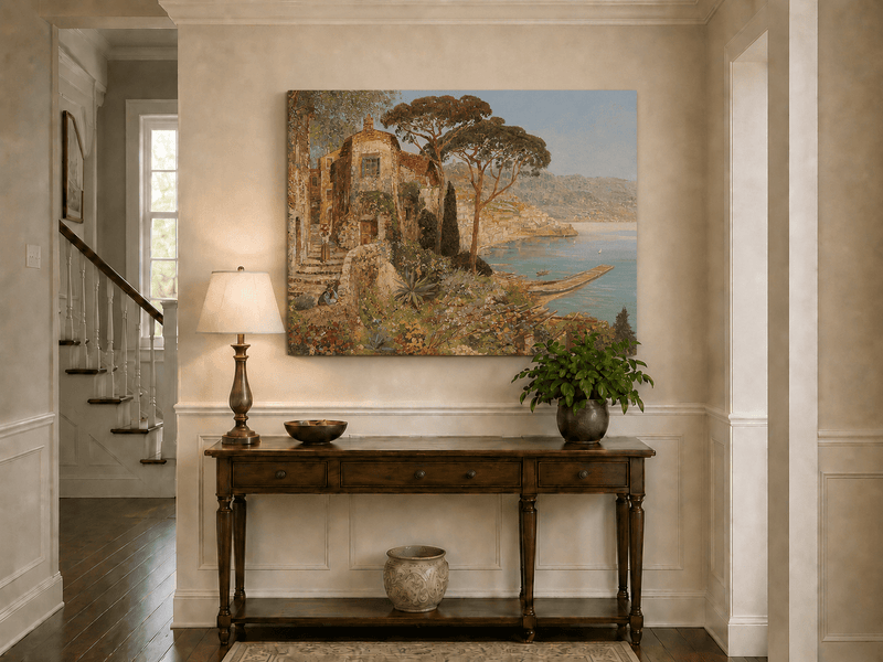 Unframed hand-painted coastal village oil painting with flowers and blue sea displayed above an entryway console table.