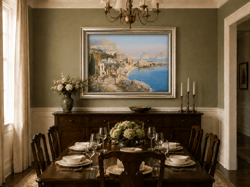 Framed hand-painted coastal village oil painting with blue sea and a rocky shoreline displayed above a formal dining table.