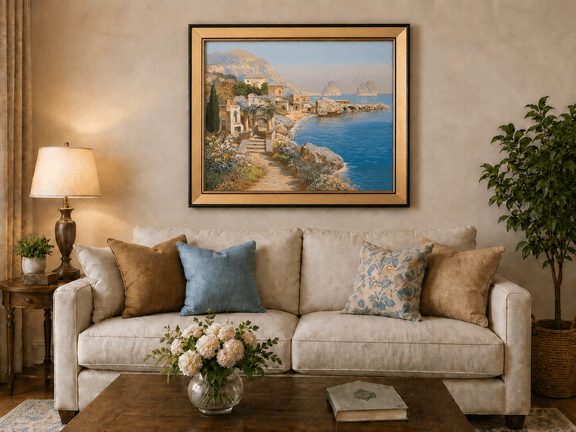 Framed hand-painted coastal village oil painting with blue sea and a rocky shoreline displayed above a neutral living room sofa.