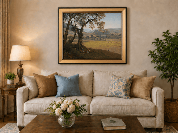 Framed hand-painted golden meadow oil painting with a picnic scene beneath a broad tree displayed above a neutral living room sofa.