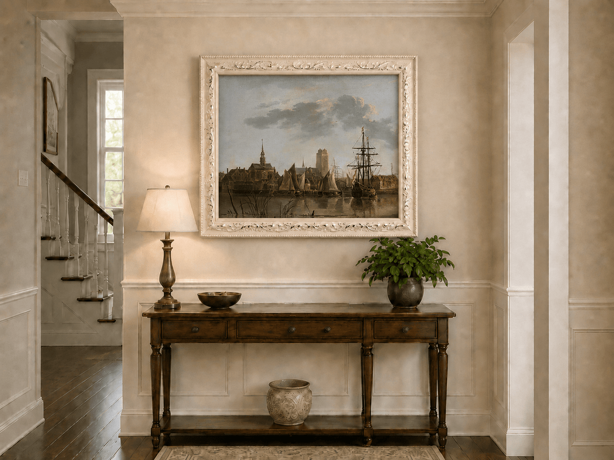 Framed hand-painted harbor view oil painting with sailing ships beneath a sunset sky displayed above an entryway console table.