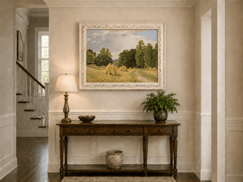 Framed hand-painted harvest field oil painting with haystacks and a tree-lined path displayed above an entryway console table.