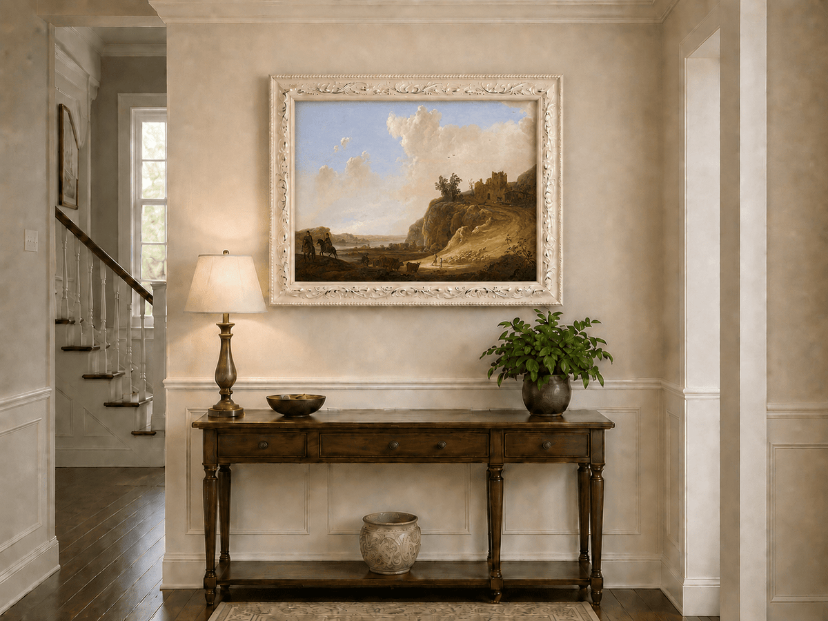 Framed hand-painted landscape oil painting with hilltop ruins, figures and a winding road displayed above an entryway console table.