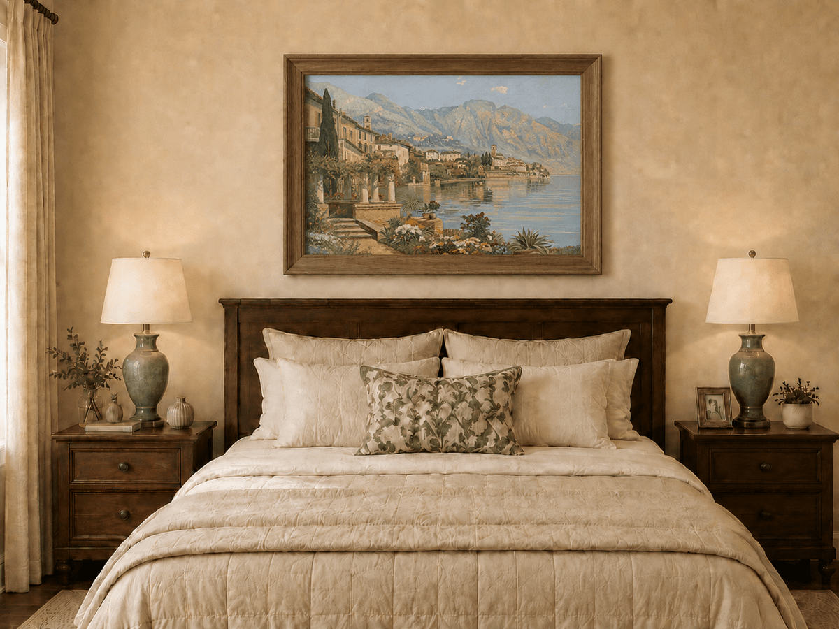 Framed hand-painted lakeside village oil painting with flowers and mountains displayed above a wooden bed in a neutral bedroom.