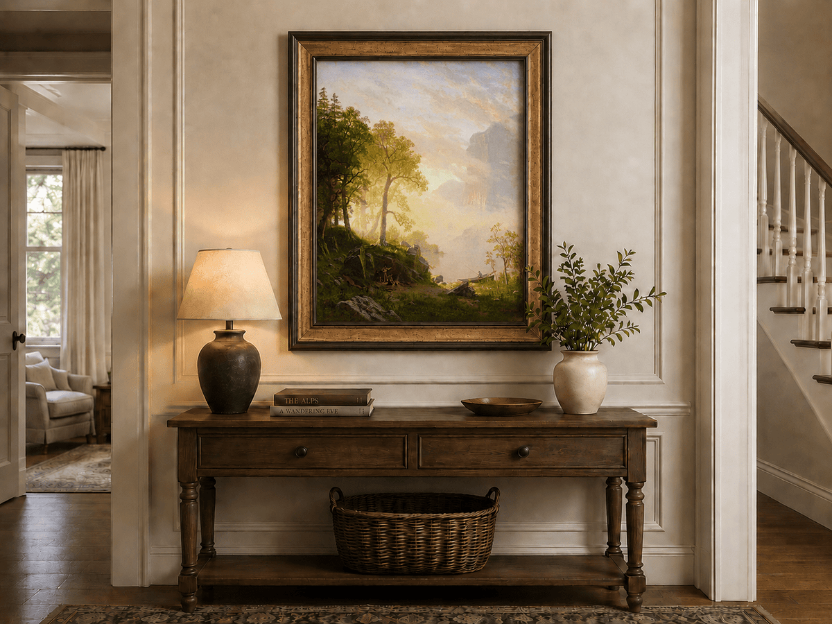Framed hand-painted lakeside woodland oil painting with a camp, angler and misty peaks displayed above an entryway console table.