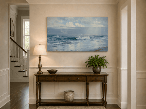 Unframed hand-painted beach oil painting with crashing waves beneath cloudy seaside skies displayed above an entryway console table.