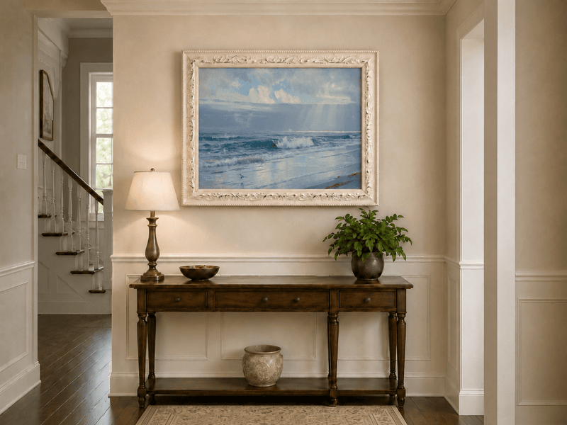 Framed hand-painted beach oil painting with crashing waves beneath cloudy seaside skies displayed above an entryway console table.