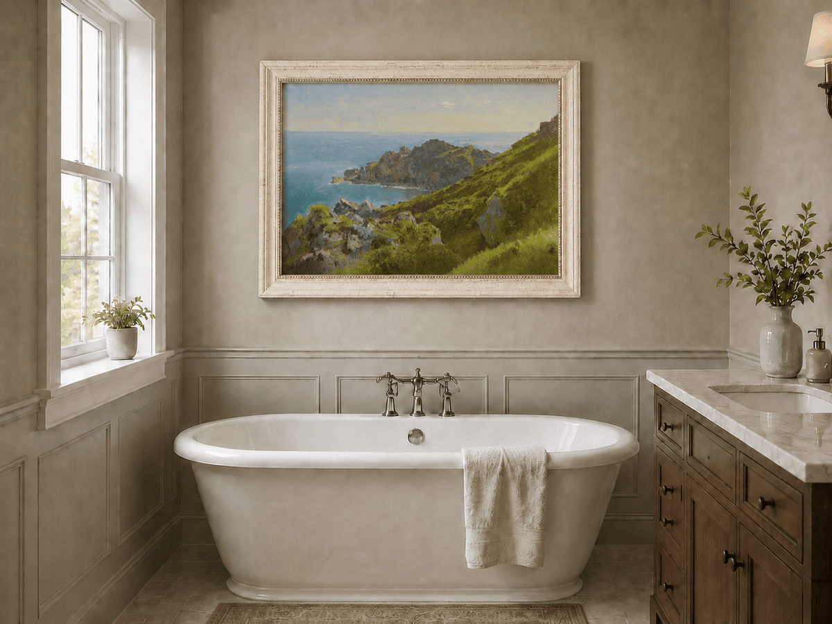 Framed hand-painted coastal landscape oil painting with green hills, rocky headland and ocean displayed above a freestanding bathtub.