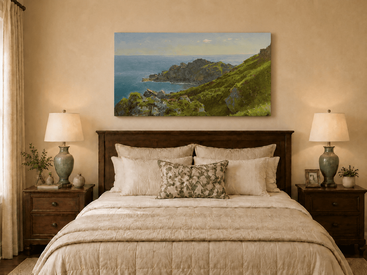 Unframed hand-painted coastal landscape oil painting with green hills, rocky headland and ocean displayed above a wooden bed in a neutral bedroom.