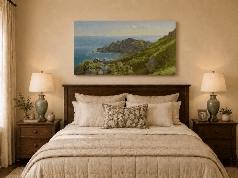 Unframed hand-painted coastal landscape oil painting with green hills, rocky headland and ocean displayed above a wooden bed in a neutral bedroom.