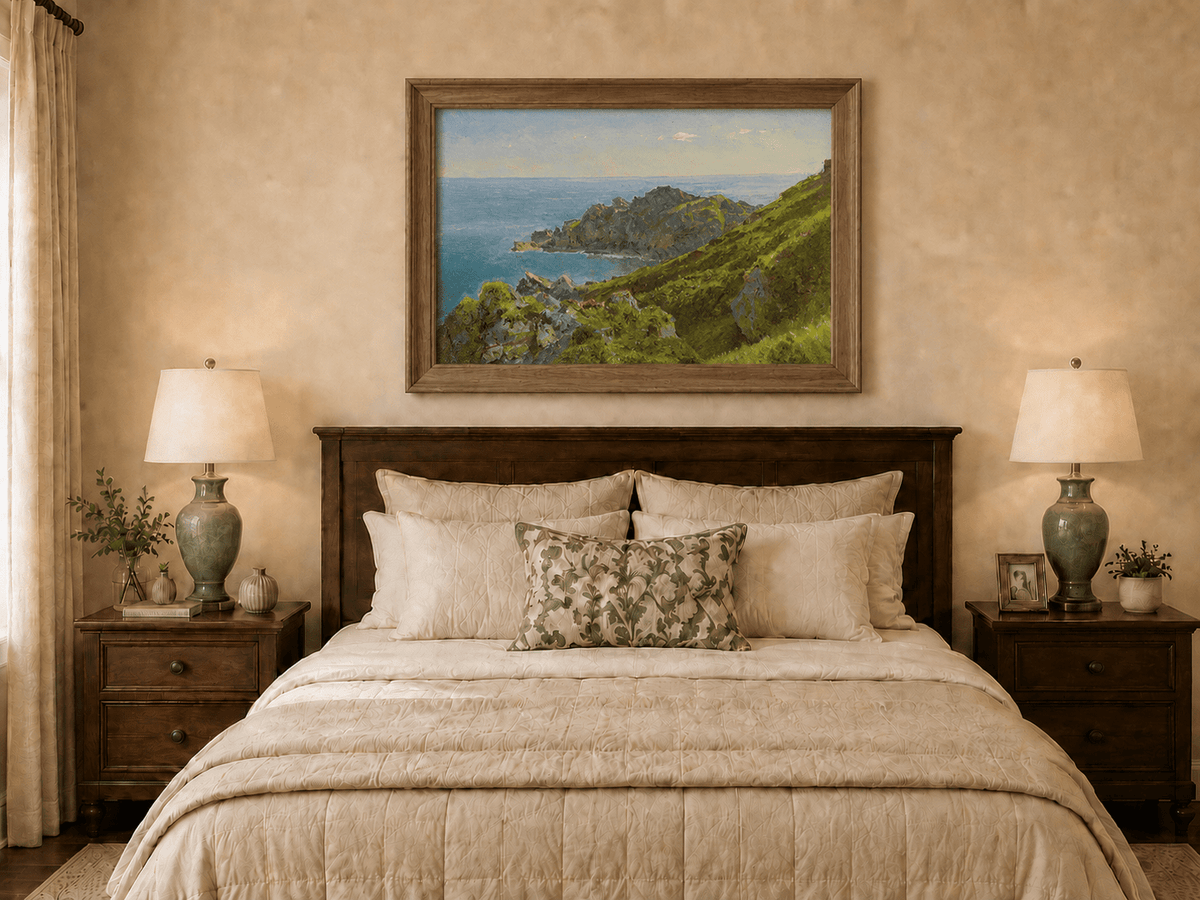 Framed hand-painted coastal landscape oil painting with green hills, rocky headland and ocean displayed above a wooden bed in a neutral bedroom.