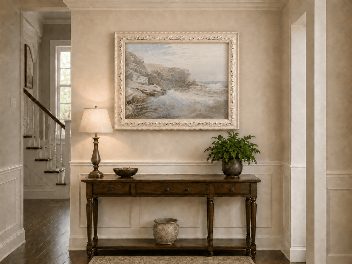 Framed hand-painted coastal cliffs oil painting with waves breaking along the rocky shore displayed above an entryway console table.